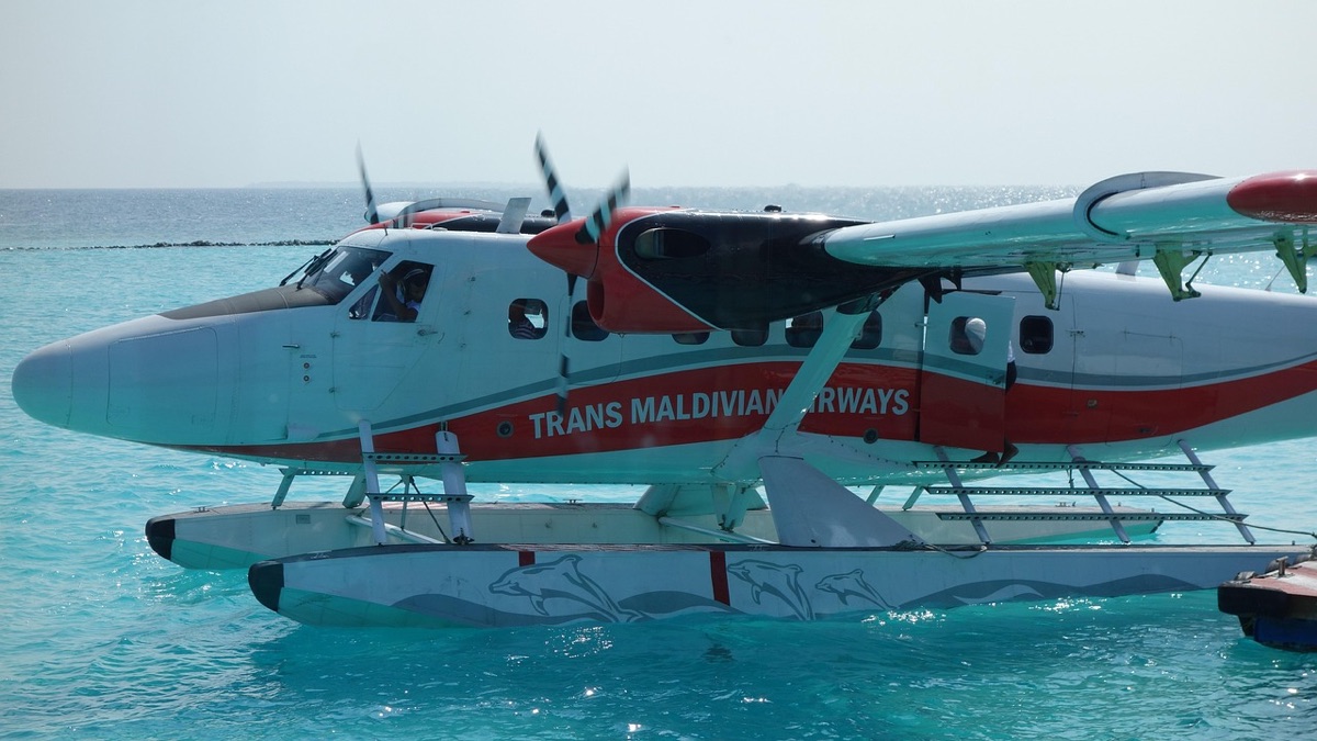 A seaplane flying over turquoise Maldivian waters towards a luxury resort